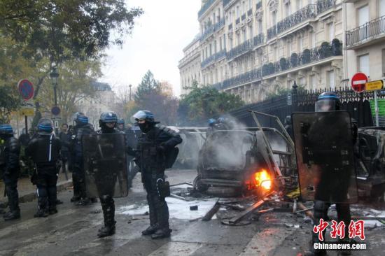 当地时间12月1日，巴黎再次发生大规模示威活动。示威者聚集在凯旋门。大批防暴警察寻求控制巴黎示威造成的混乱局面。图为防暴警察在巴黎市中心正在燃烧的车辆前严密警戒。 记者 李洋 摄